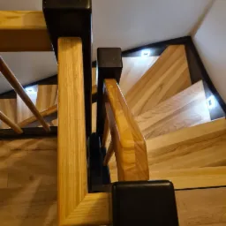 Drewniane schody z podświetleniem LED, czarne balustrady, widok z g&oacute;ry.