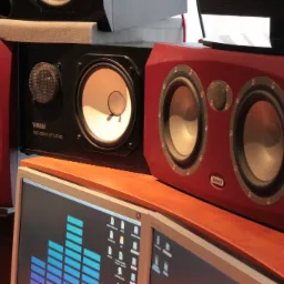 Para czerwonych głośników marki Tannoy i czarny głośnik Yamaha NS-10M Studio, ustawione obok monitorów z wyświetlonym oknem programu do edycji dźwięku.