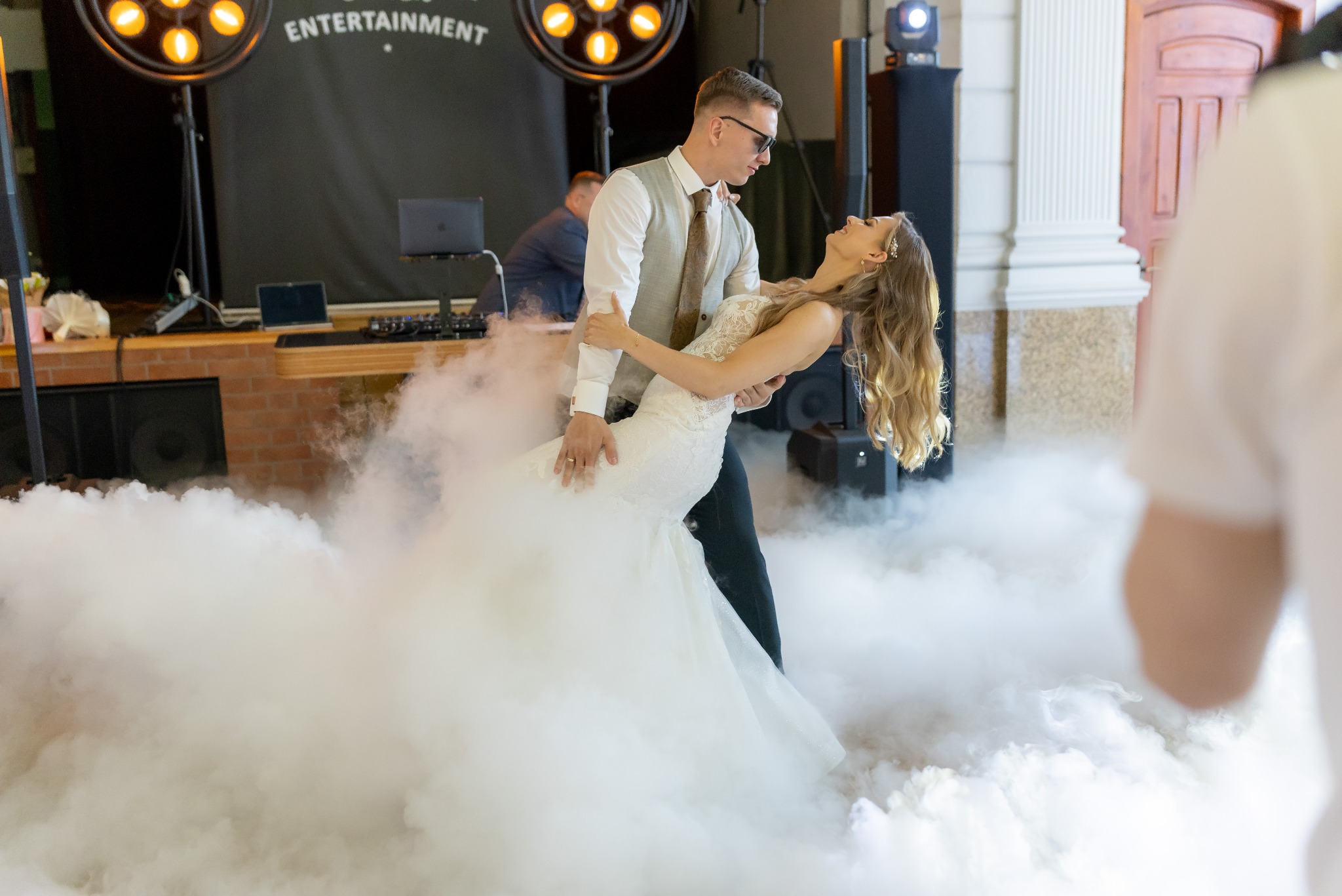 Para młoda tańczy pierwszy taniec w chmurze dymu na tle sceny z oświetleniem eventowym.