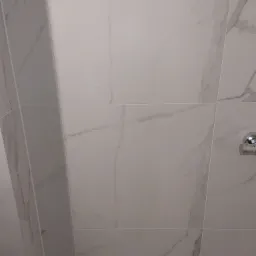 Białe, marmurowe płytki ścienne w łazience, z widocznym chromowanym uchwytem na papier toaletowy po prawej stronie.