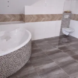 Nowoczesna łazienka w trakcie wykańczania: mozaika na obudowie wanny, brązowe płytki podłogowe, biała armatura, dekoracyjne pasy płytek na ścianach.