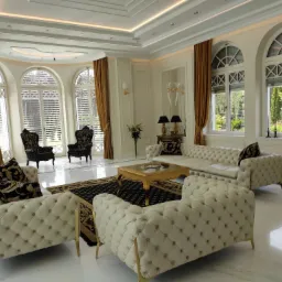 Elegancki salon w stylu glamour z białymi sofami Chesterfield, złotymi akcentami i oknami łukowymi z widokiem na ogród.