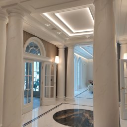 EL-TOM Karol Tomczyk - Eleganckie wnętrze z marmurowymi kolumnami, oświetleniem sufitowym i otwartymi drzwiami na zewnątrz.