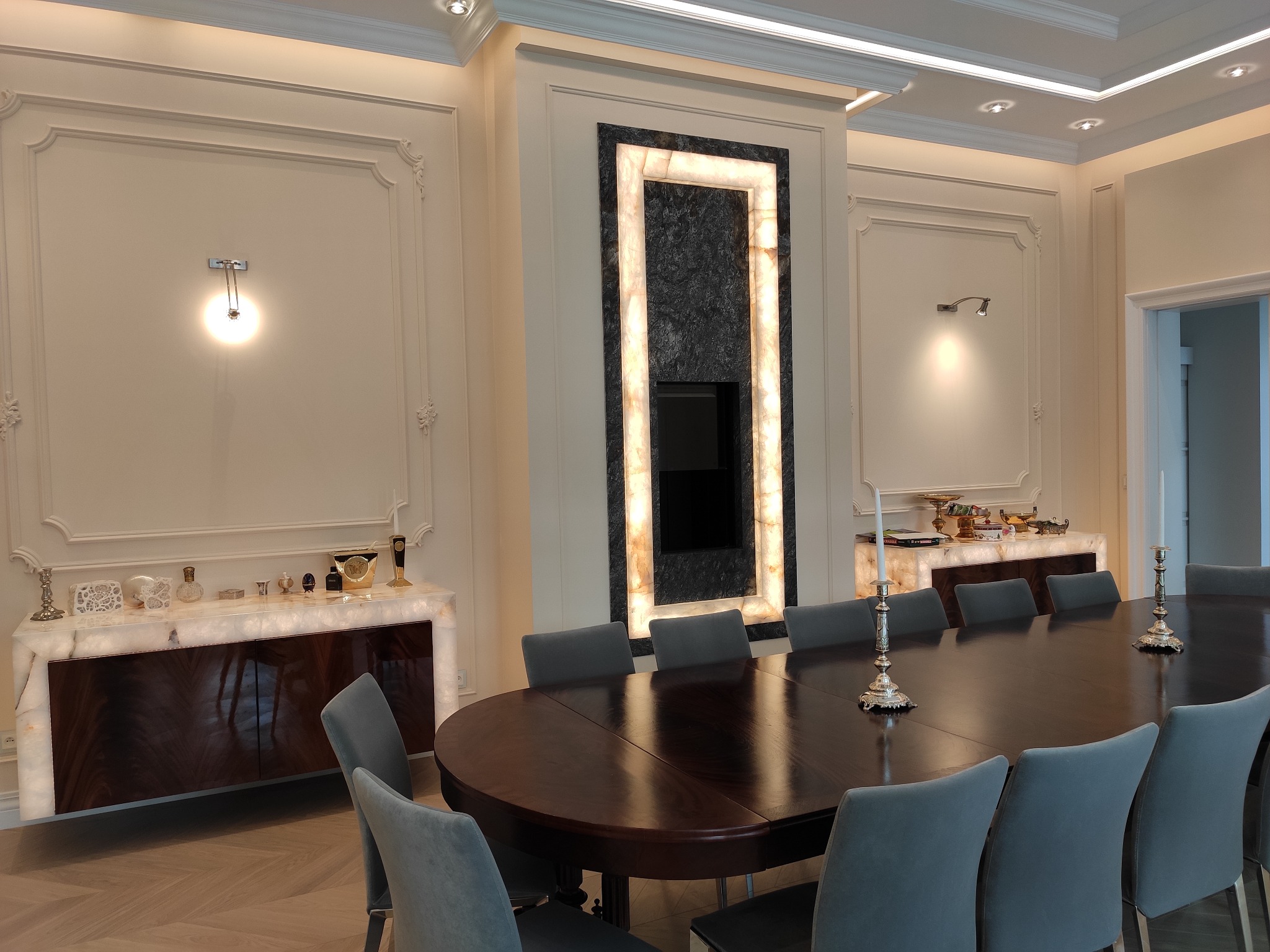 Elegancka jadalnia z podświetlanymi meblami i dekoracyjnym oświetleniem ściennym, centralnie umieszczony telewizor otoczony podświetlaną ramą z onyksu.