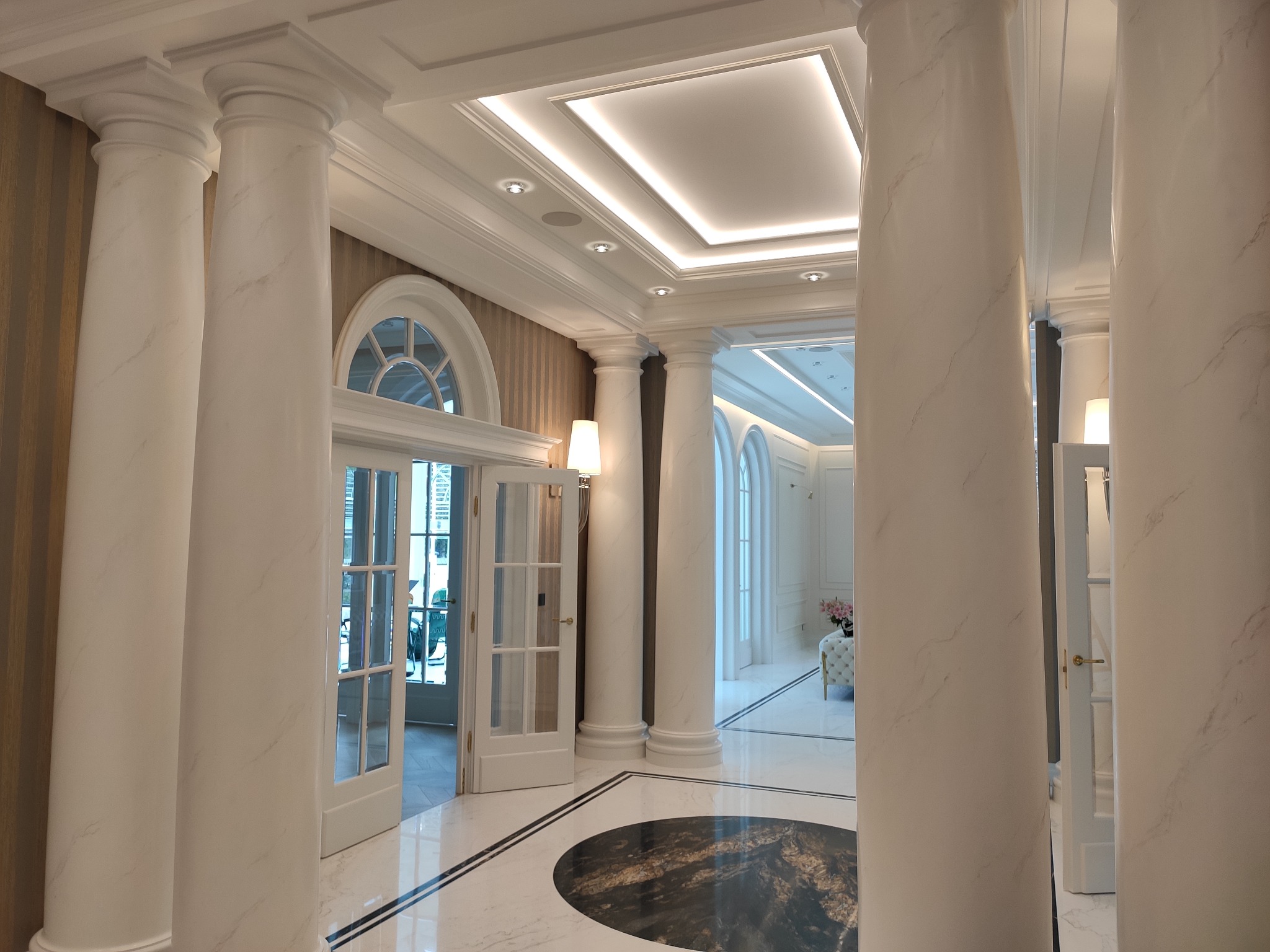 Eleganckie wnętrze z marmurowymi kolumnami, oświetleniem sufitowym i otwartymi drzwiami na zewnątrz.