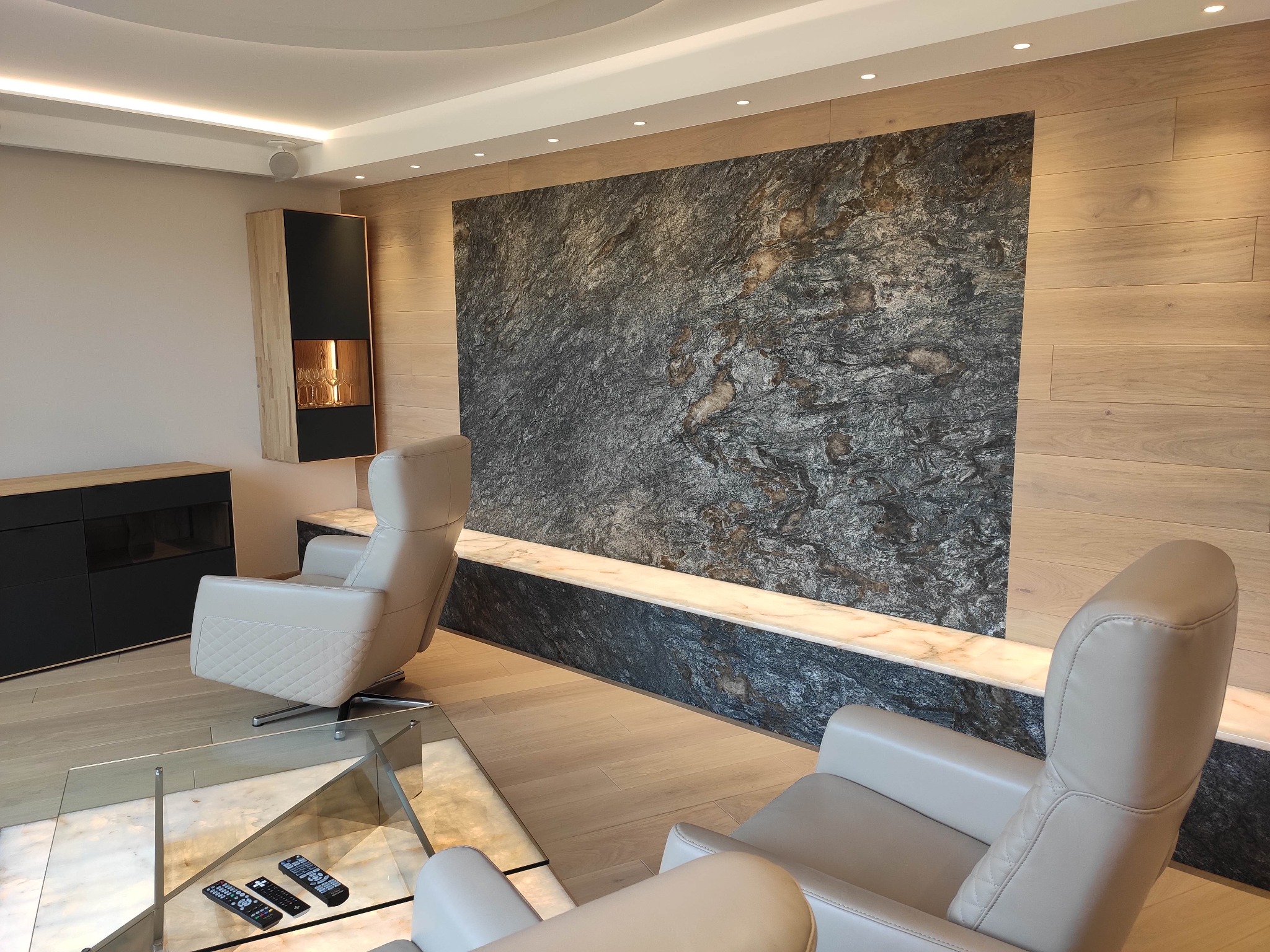 Salon z nowoczesnym oświetleniem punktowym, kamienną ścianą akcentującą i beżowymi fotelami obrotowymi.