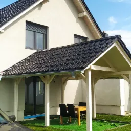 Dom jednorodzinny z nowym, czarnym dachem ceramicznym i osłoniętym tarasem z drewnianą konstrukcją, widok z poziomu trawnika, fragment samochodu na pierwszym planie.