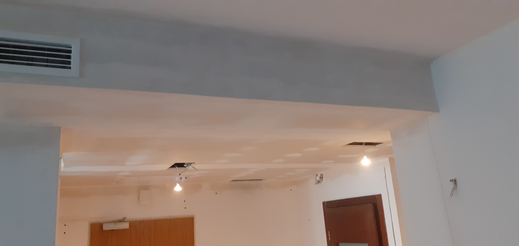 Sufit z zamontowaną kratką wentylacyjną i otworami na oświetlenie w trakcie prac wykończeniowych, widoczne ślady szpachlowania i niedomalowane ściany.