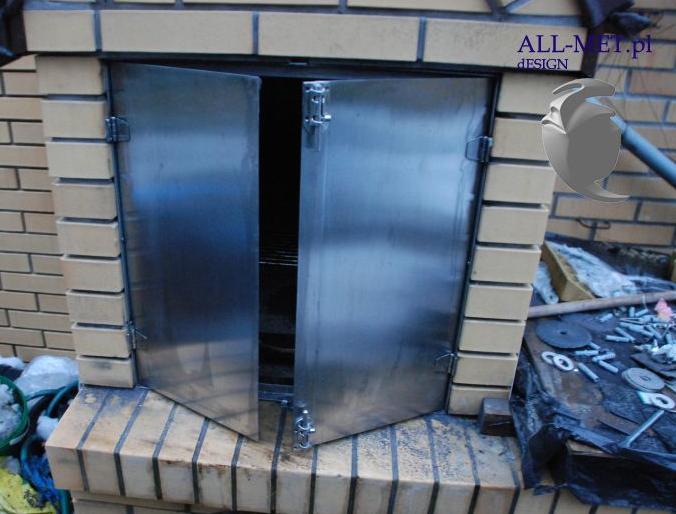 Otwarta, dwuskrzydłowa, stalowa klapa pieca w obudowie z cegieł, z widocznym wnętrzem paleniska i narzędziami obok.