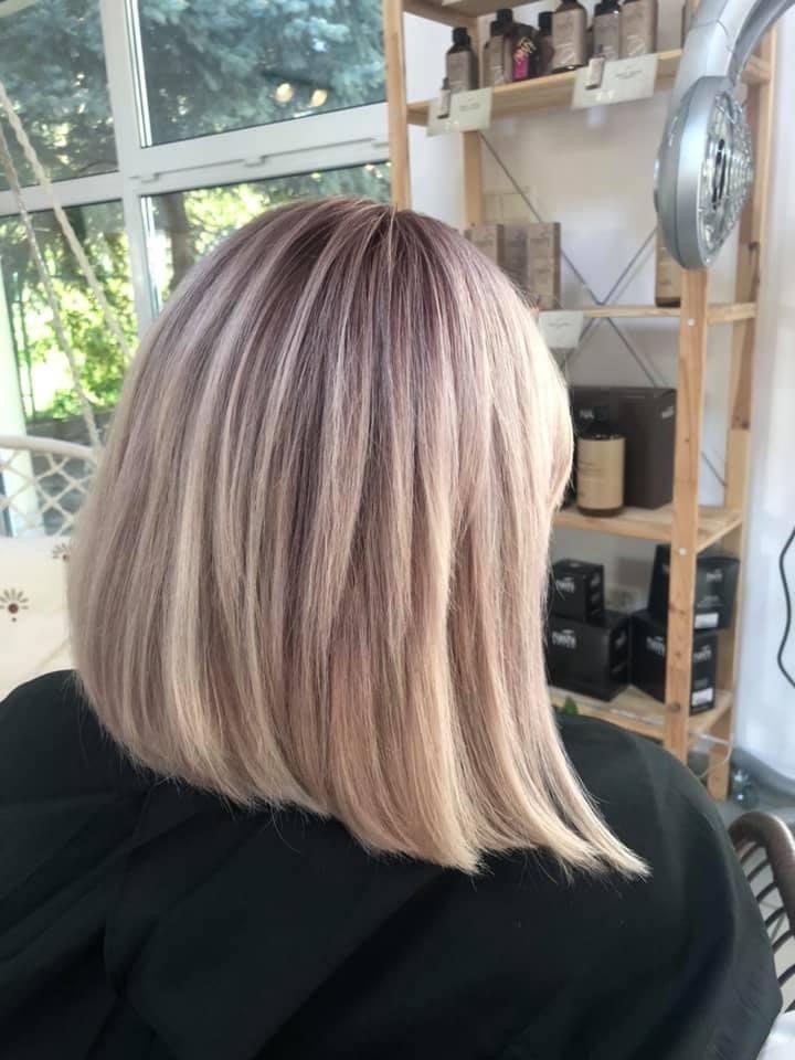 Świeżo ostrzyżone, wycieniowane włosy w odcieniach blondu i fioletu, widok z tyłu na tle jasnego wnętrza salonu.