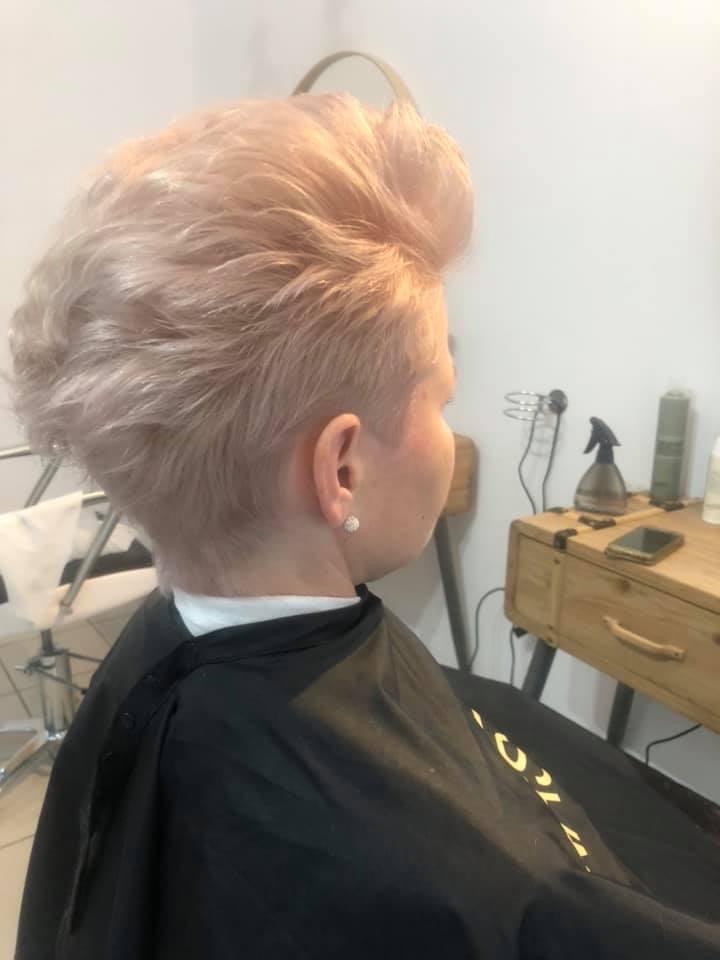 Krótkie, platynowe włosy z podgolonymi bokami, zaczesane do góry, widok z profilu, klientka w czarnej pelerynie.