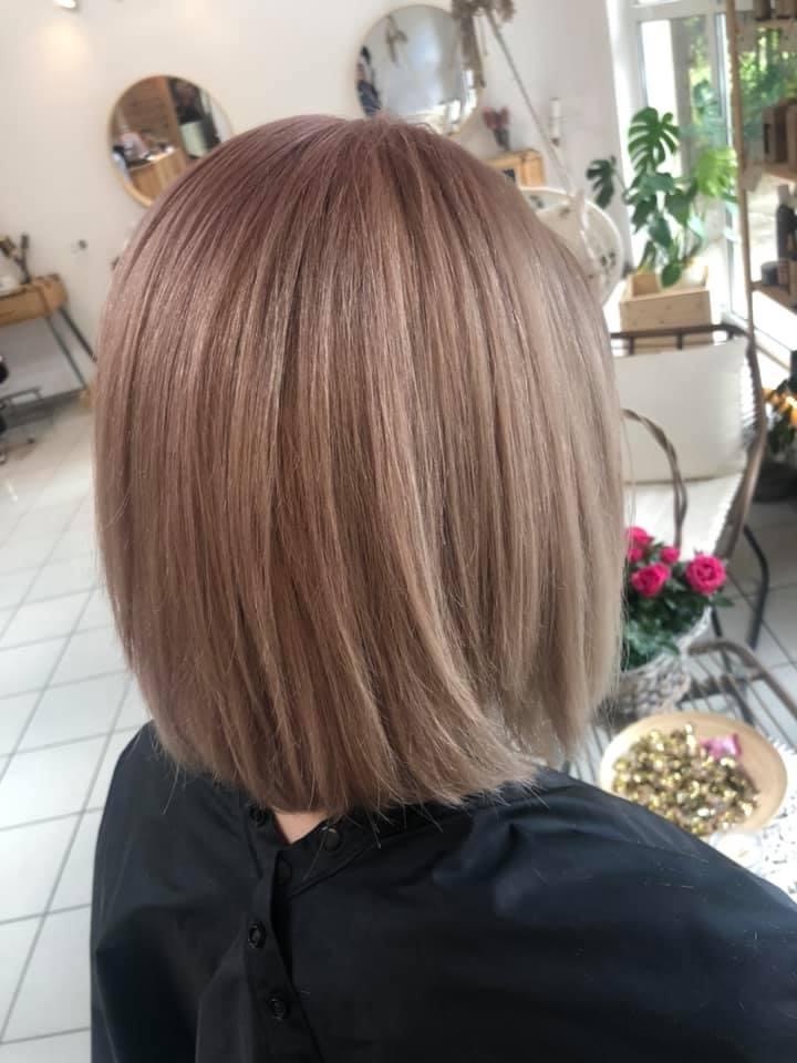 Świeżo ostrzyżone, proste bob z koloryzacją sombre w odcieniach różowego złota i chłodnego blondu, widok z tyłu, czarny fartuch ochronny.