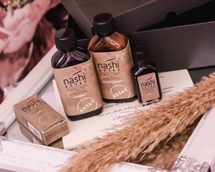 Zestaw kosmetyków Nashi Argan: szampon, odżywka i olejek, zapakowane w eleganckie pudełko z dekoracyjnym piórem.