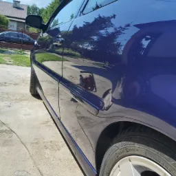 Błyszczący, granatowy bok samochodu po polerowaniu, z widocznym odbiciem otoczenia i fragmentem aluminiowej felgi.