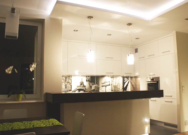 Nowoczesna aranżacja kuchni w Gdańsku z białymi meblami na wysoki połysk, czarnym blatem i dekoracyjnym panelem szklanym z motywem Paryża.