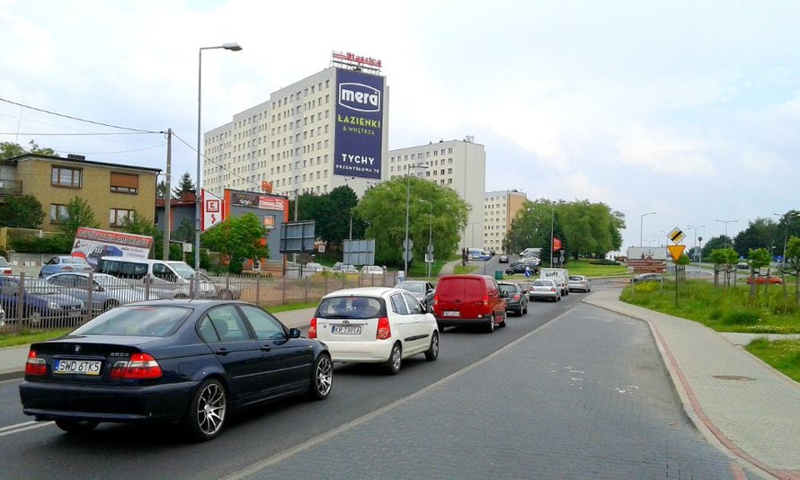 Billboard reklamowy na budynku mieszkalnym z napisem 'mera ŁAZIENKI I WNĘTRZA TYCHY' widoczny z ulicy z ruchem samochodowym.