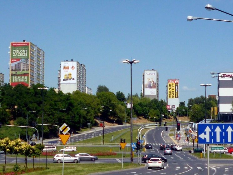 Billboardy reklamowe na budynkach widoczne z ruchliwej ulicy miejskiej w słoneczny dzień.