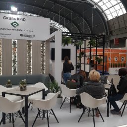 Brand Creation Sp.j - Stoisko targowe firmy Grupa KPID z panelami dekoracyjnymi z kamienia naturalnego, stoliki kawowe z białymi krzesłami i roślinami, widoczni zwiedzający.