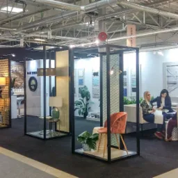 Aranżacja stoiska targowego z ekspozycją łazienek i elementów wyposażenia wnętrz, w tym umywalki, armatura, oświetlenie i płytki ceramiczne, z widocznymi osobami w tle.