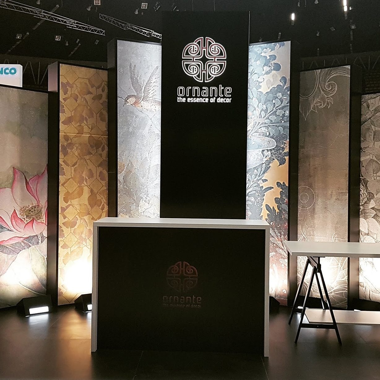 Stoisko targowe z panelami dekoracyjnymi marki Ornante, prezentujące różne wzory i tekstury, w tym motywy kwiatowe i abstrakcyjne, oświetlone od dołu, z widocznym logo firmy na czarnym tle.