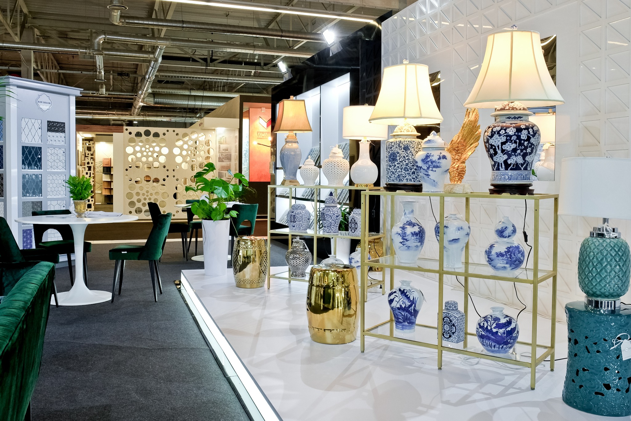 Aranżacja ekspozycyjna z dekoracyjnymi wazonami i lampami w stylu chinoiserie, ustawionymi na złotych regałach i stolikach, w tle panele ścienne z geometrycznym wzorem.