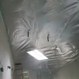 Poddasze w trakcie ocieplania folią termoizolacyjną, widoczne drabiny i rusztowanie, okno dachowe w tle.