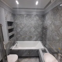 Nowoczesna łazienka w odcieniach szarości z marmurkowymi płytkami, geometrycznym wzorem na ścianach, białą wanną i umywalką, oraz grzejnikiem drabinkowym.