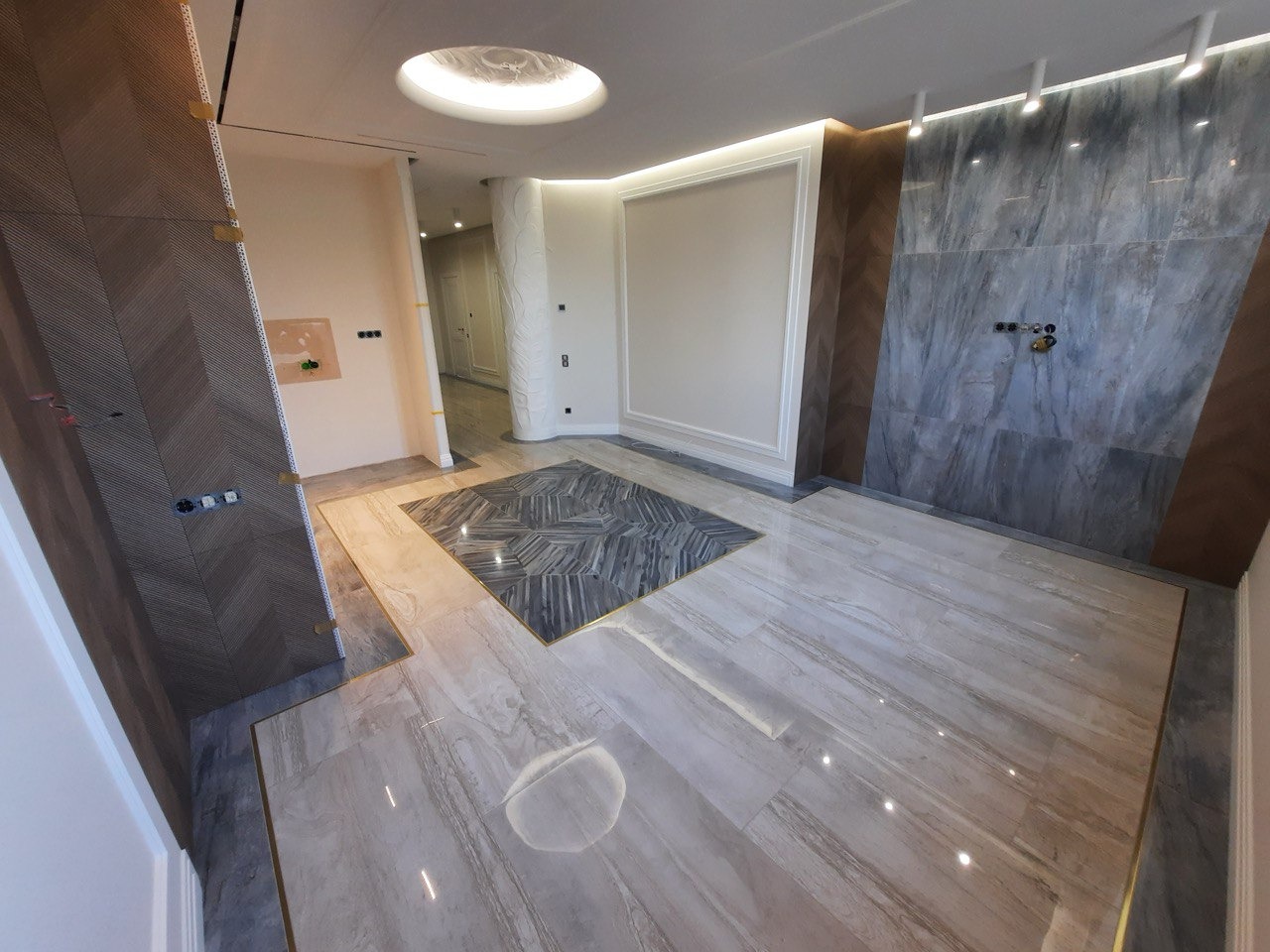 Ekskluzywne wnętrze w trakcie wykańczania: marmurowe płytki podłogowe w odcieniach beżu i szarości z dekoracyjnym wzorem geometrycznym, ściana wyłożona płytkami imitującymi marmur, oświetlenie...