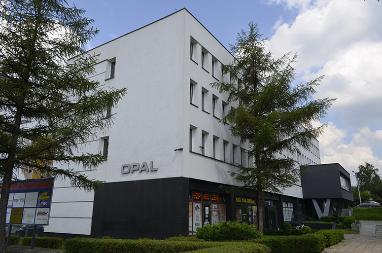Nowoczesny, trzypiętrowy budynek biurowy z białymi ścianami i czarnym parterem, z napisem 'OPAL' na elewacji, otoczony zielenią.