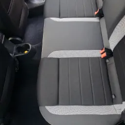 Wnętrze samochodu z widoczną tylną kanapą w odcieniach szarości, z detalami w postaci pasów bezpieczeństwa i uchwytu na napoje z żółtym elementem w środku.