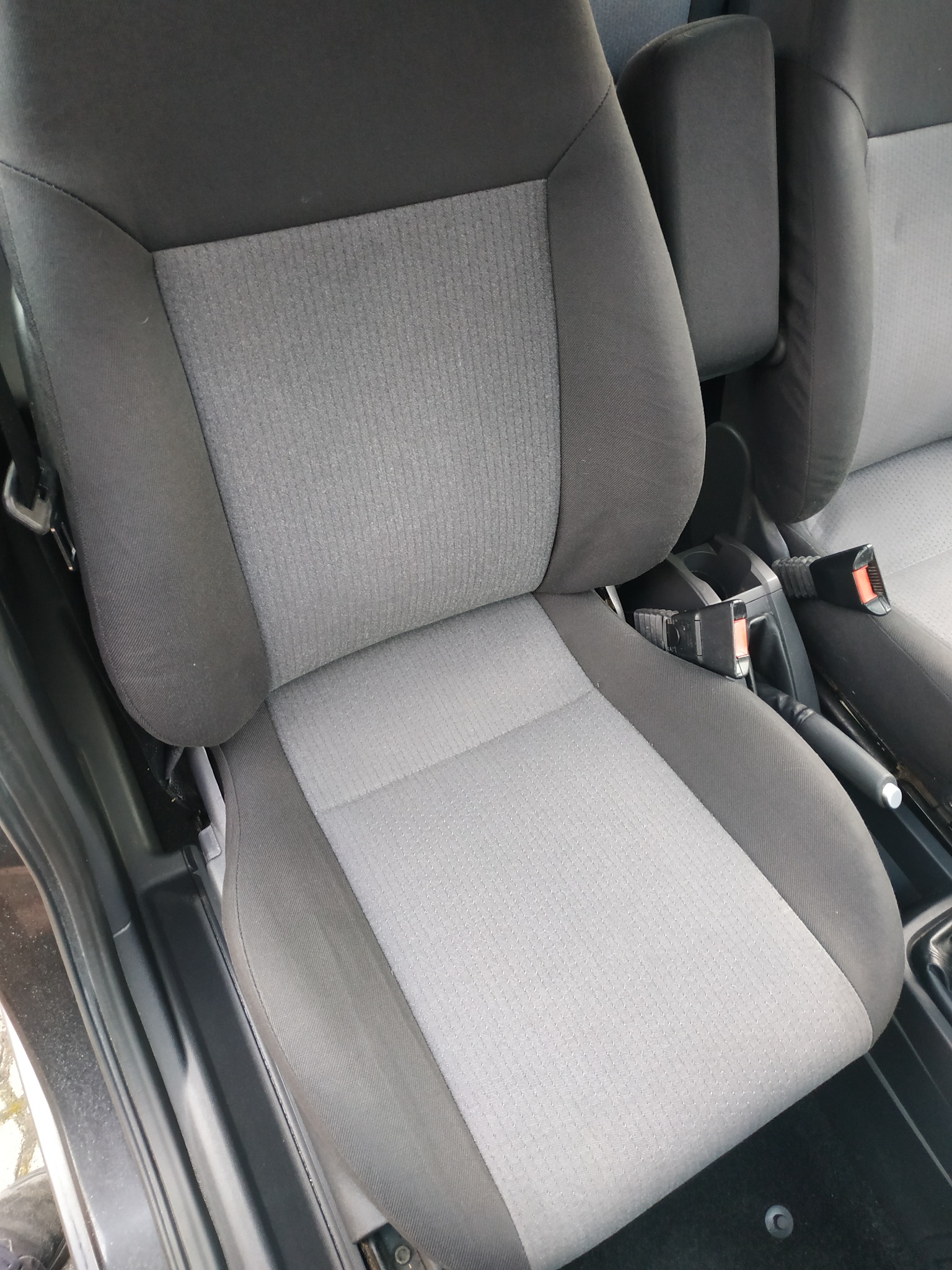 Szare, materiałowe siedzenie samochodowe z widocznym pasem bezpieczeństwa i konsolą środkową.