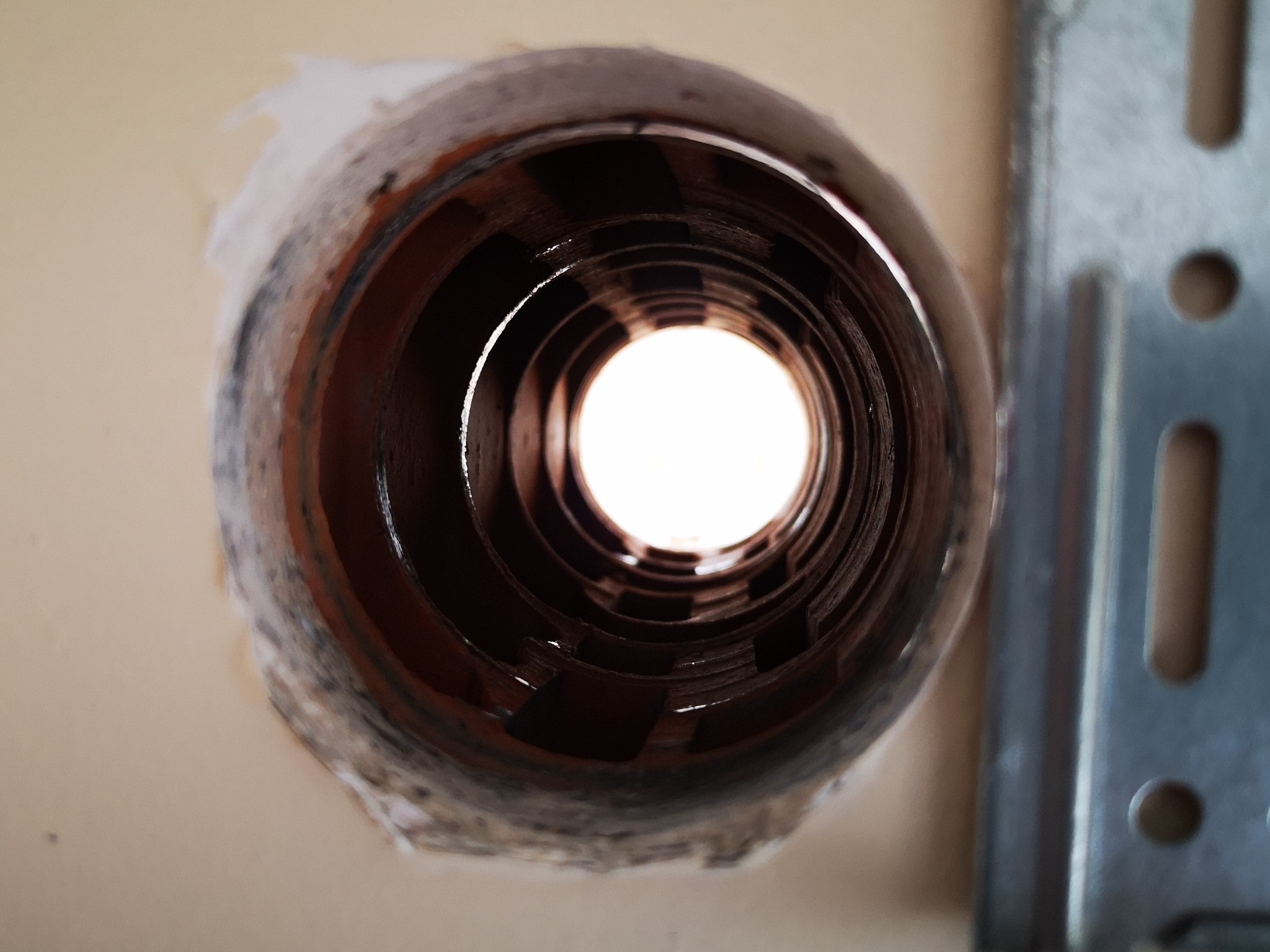 Otwór w ścianie z widoczną rurą instalacyjną, prawdopodobnie przygotowany do montażu klimatyzacji. Fragment metalowego wspornika po prawej stronie.