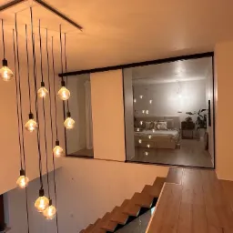 Nowoczesne wnętrze z drewnianymi schodami, wiszącymi lampami i przeszkleniem oddzielającym sypialnię, widok z góry.