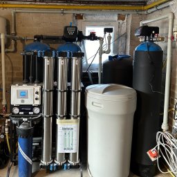 Drill Solutions Sp. Zo.o. - Zestaw urządzeń do filtracji wody z kilkoma cylindrycznymi filtrami ze stali nierdzewnej, zbiornikiem z tworzywa sztucznego i elektronicznym sterownikiem, zainstalowany w pomieszczeniu z ceglanymi...