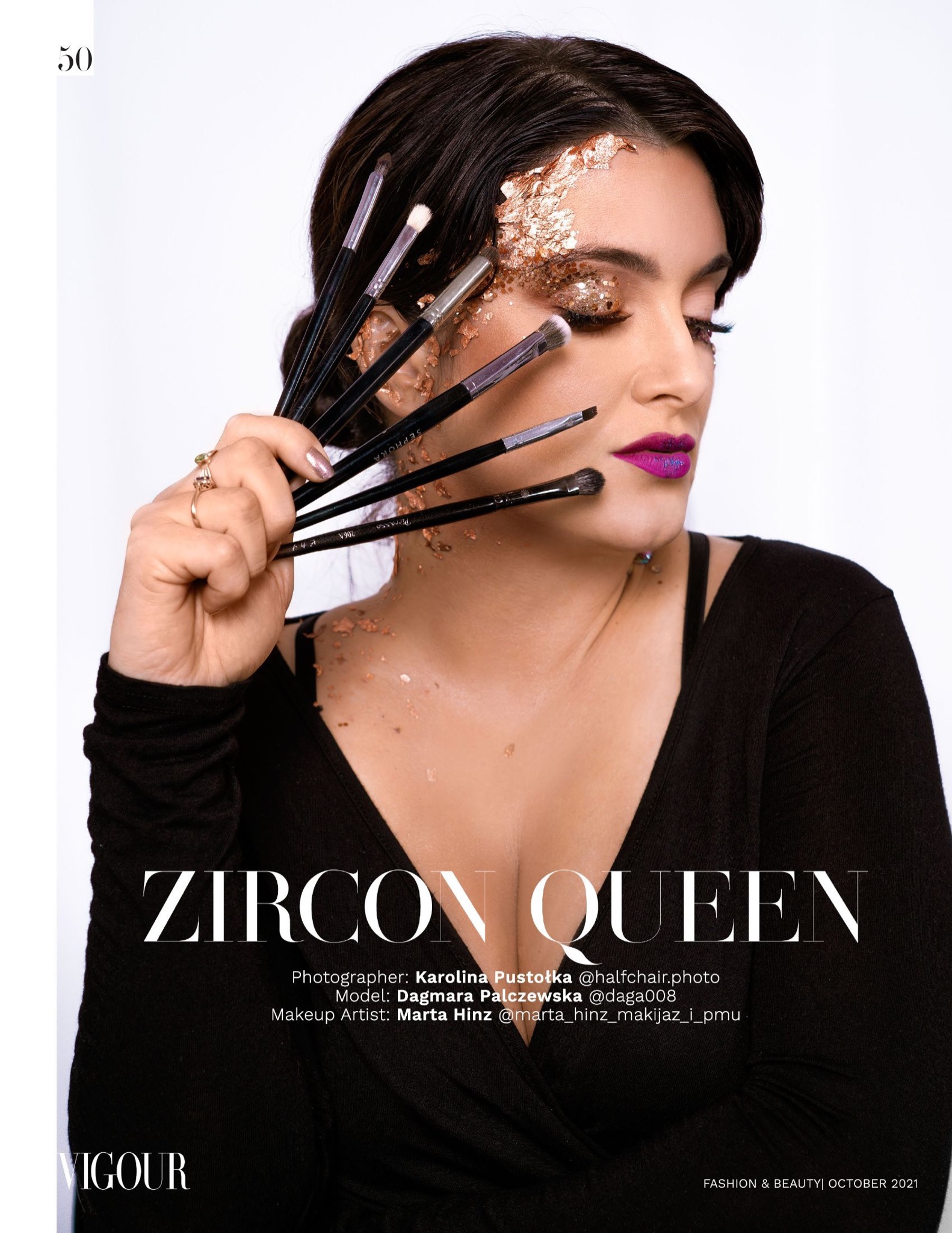 Portret kobiety z intensywnym makijażem, złotymi płatkami na twarzy i powiekach, trzymającej pędzle do makijażu blisko twarzy, z widoczną nazwą marki na jednym z pędzli.