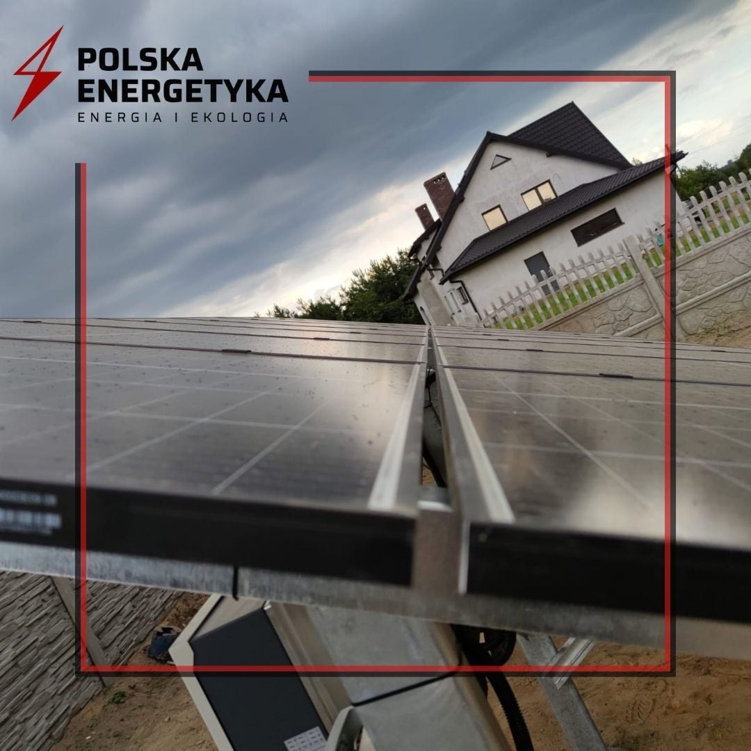 Panele słoneczne na dachu domu jednorodzinnego pod pochmurnym niebem, widoczne logo firmy Polska Energetyka.