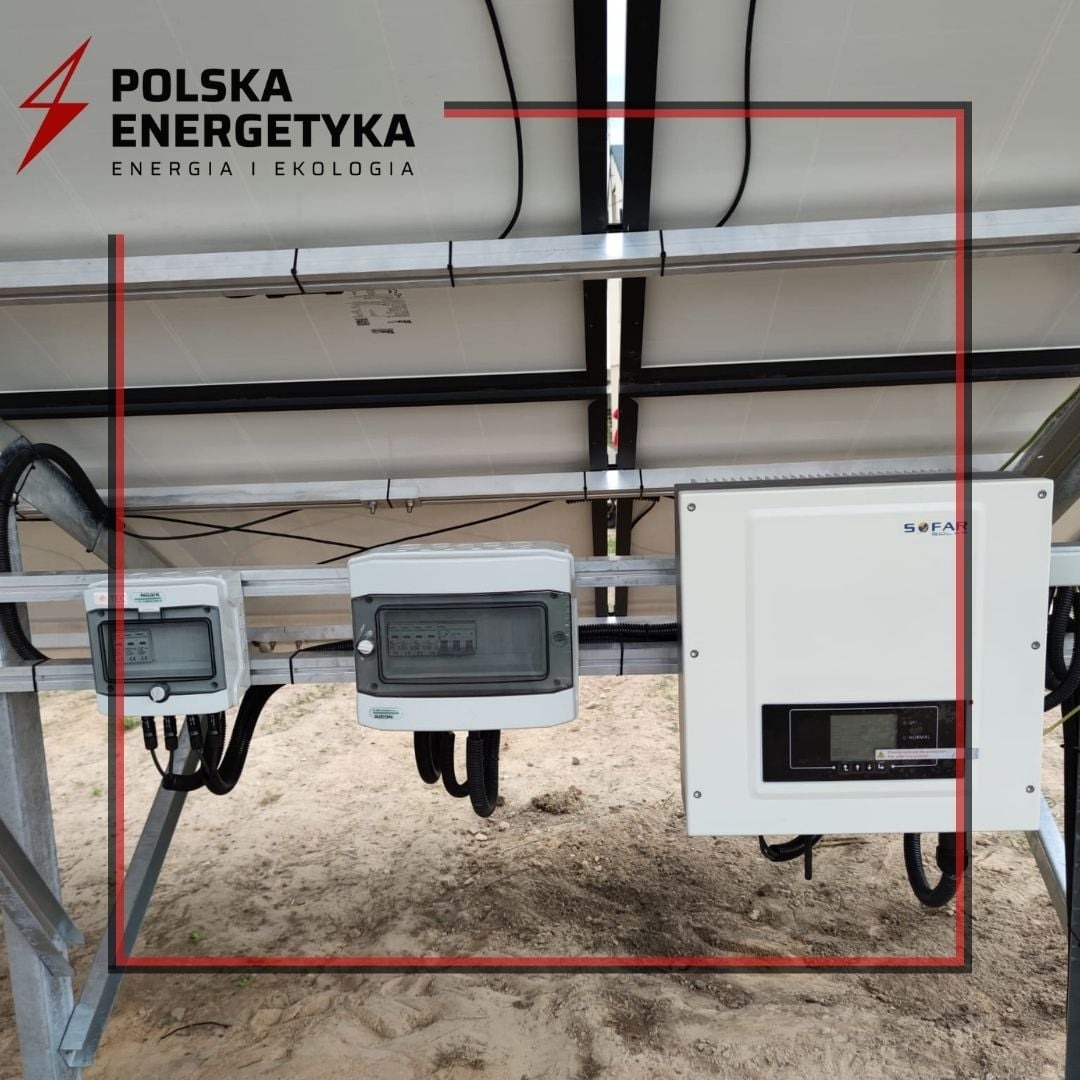 Widok od spodu na panele słoneczne z zainstalowanym inwerterem Sofar i skrzynkami elektrycznymi, widoczne przewody i elementy konstrukcyjne.