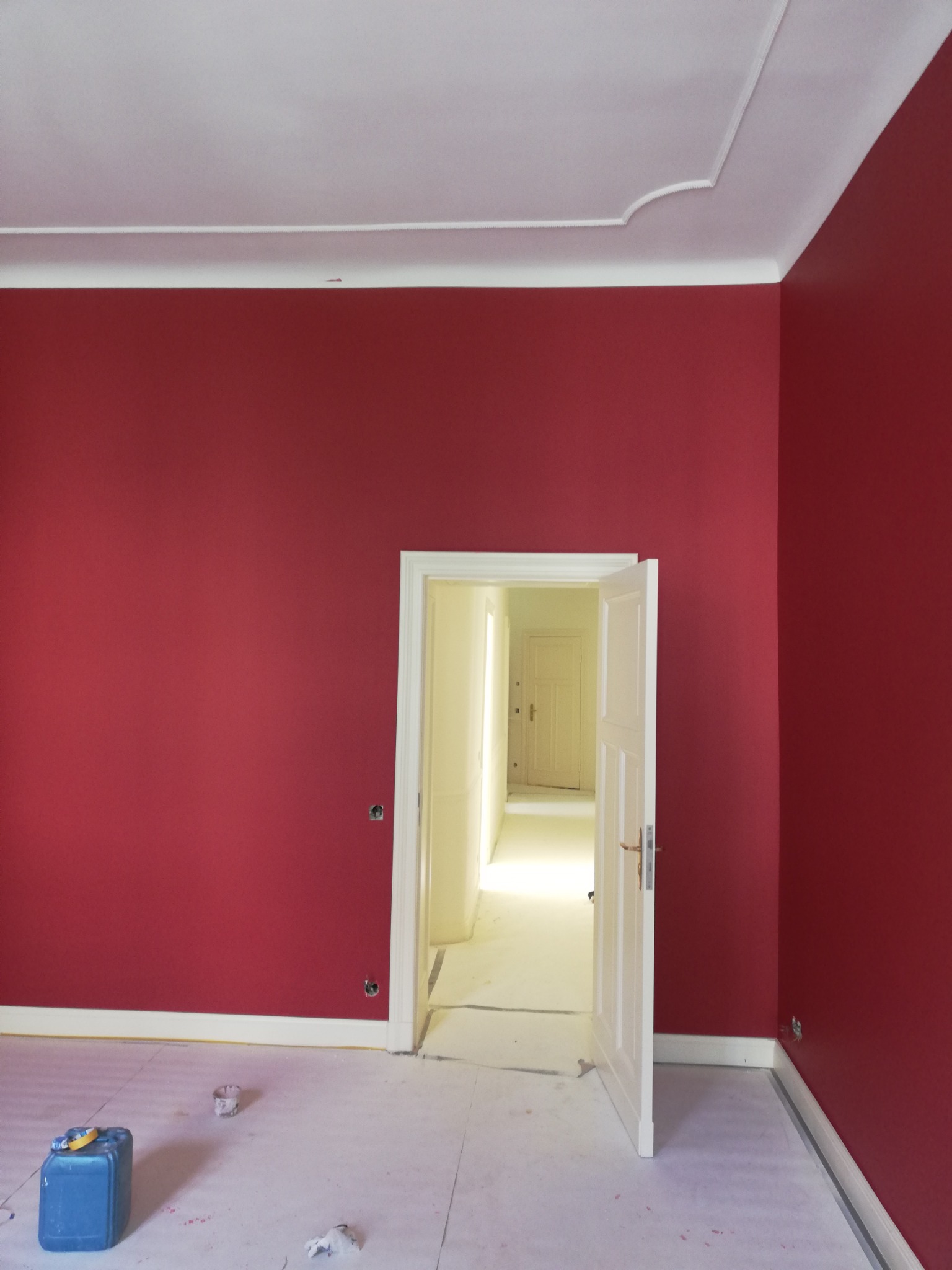 Pomieszczenie w Gorzowie Wielkopolskim po malowaniu ścian na intensywny czerwony kolor, z widocznymi śladami zabezpieczeń podłogi i otwartymi drzwiami do kolejnego, jasnego pokoju.