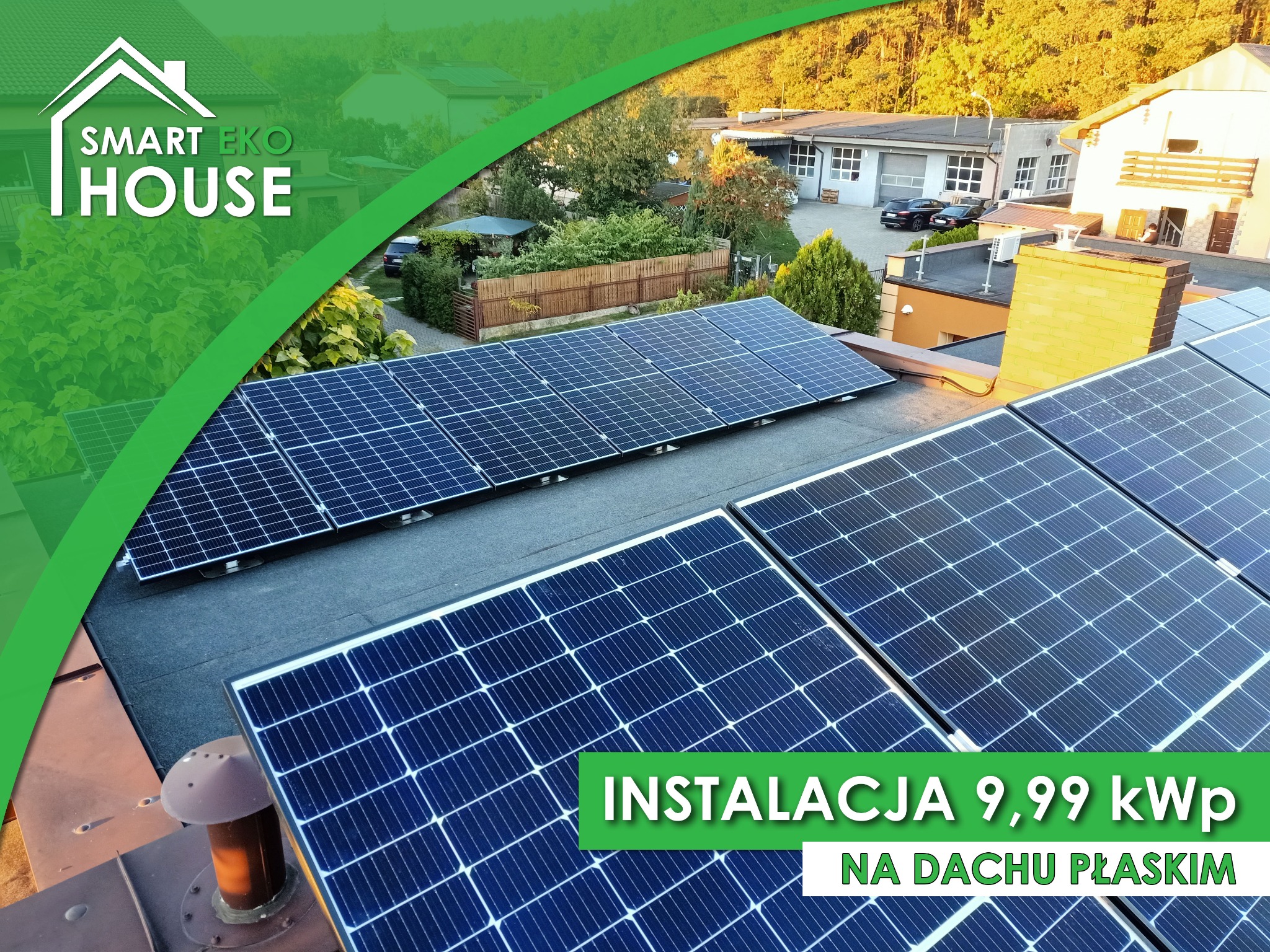 Instalacja paneli fotowoltaicznych o mocy 9,99 kWp na płaskim dachu budynku z kominem, widok z góry na tle zabudowy i zieleni.