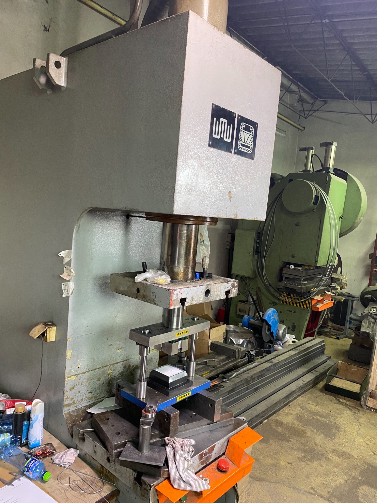 Duża, przemysłowa prasa mechaniczna w hali produkcyjnej, z widocznymi elementami roboczymi i otoczeniem warsztatowym.