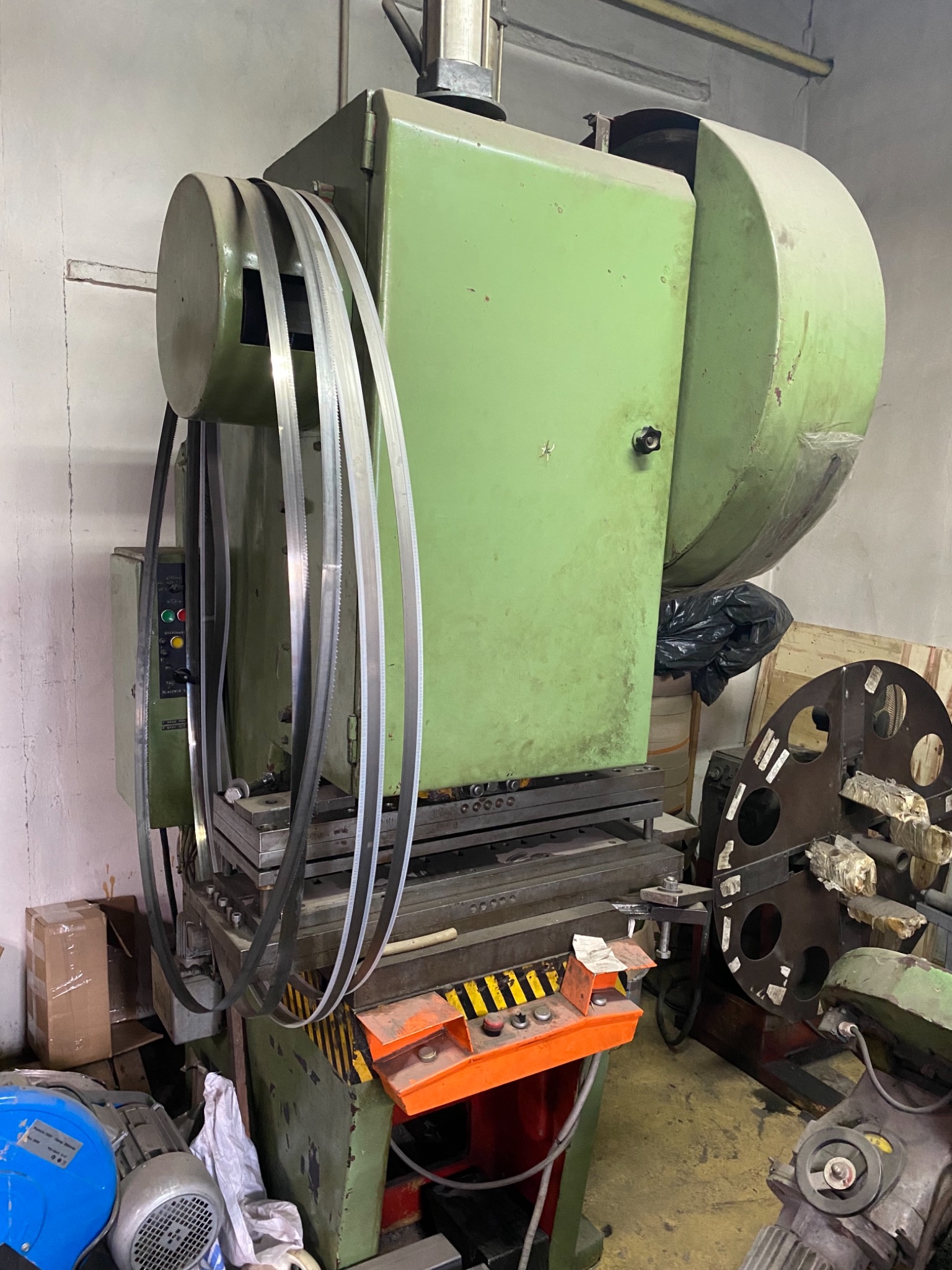 Zielona, przemysłowa piła taśmowa do metalu z widocznymi ostrzami, panelem sterowania i elementami hydraulicznymi w warsztacie.