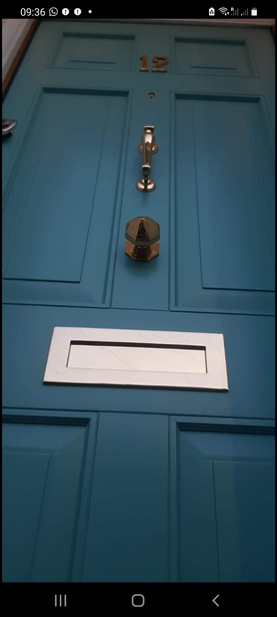 Turkusowe drzwi wejściowe z numerem 12, złotą kołatką, wizjerem i skrzynką na listy.