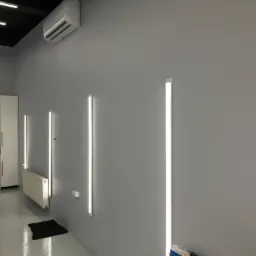 Szare wnętrze po malowaniu z zamontowanymi pionowymi panelami LED, klimatyzacją, grzejnikiem i białymi szafkami.