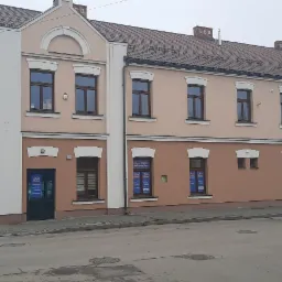 Dwukondygnacyjny budynek szkoły językowej z reklamami w oknach, widok z ulicy w pochmurny dzień.