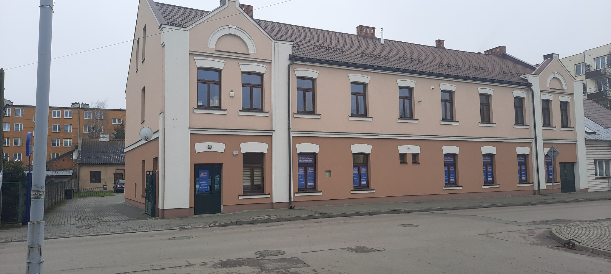 Dwukondygnacyjny budynek szkoły językowej z reklamami w oknach, widok z ulicy w pochmurny dzień.