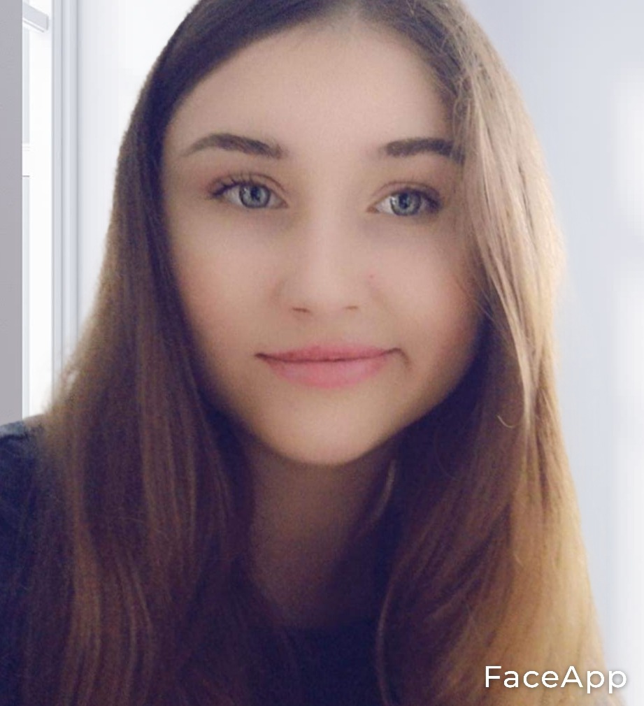 Portret młodej kobiety z długimi, brązowymi włosami i jasnymi oczami, uśmiechająca się delikatnie, z efektem wygładzenia skóry z aplikacji FaceApp.