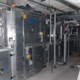 Rozbudowana instalacja wentylacyjna Klimor z rurami i przewodami w surowym pomieszczeniu technicznym.