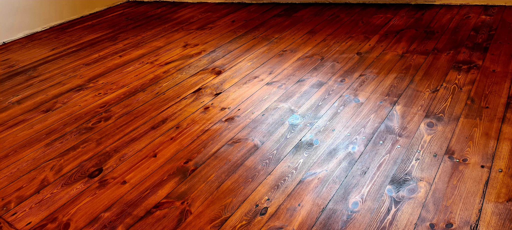 Wycyklinowana podłoga z desek pomalowana na ciemny brąz z widocznymi śladami po szpachlowaniu dziur po gwoździach.