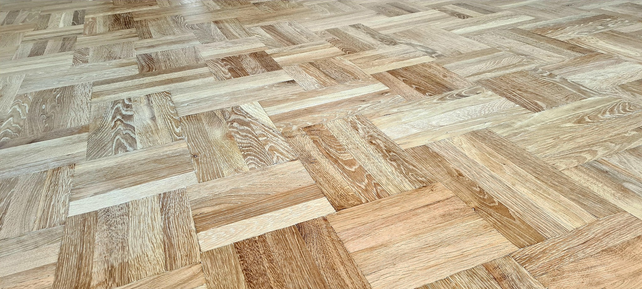 Jasny parkiet ułożony we wzór jodełki francuskiej, widoczne naturalne usłojenie drewna i subtelne różnice w odcieniach poszczególnych klepek.