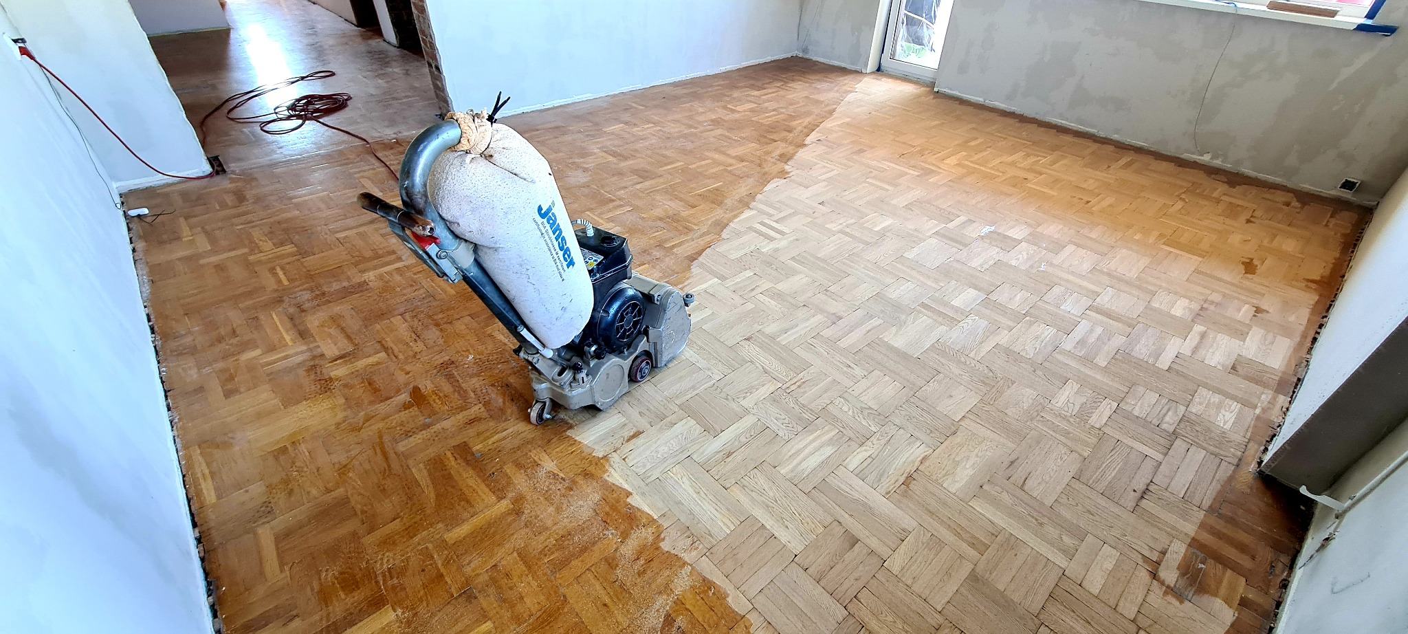 Cyklinowanie parkietu ułożonego w jodełkę: maszyna do cyklinowania w trakcie pracy, widoczna różnica w kolorze między obszarem obrobionym a nieobrobionym.